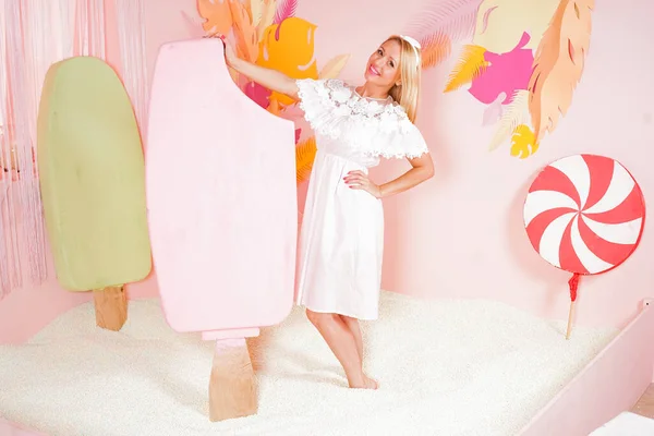 Charmante vrolijke blonde vrouw in een zachte kant zomer jurk poseren met een enorme roze ijs in het zwembad met schuim zachte kleine ballen en bezig met ontspanningstherapie. — Stockfoto