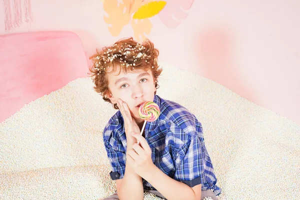 Adolescente chico en la piscina con espuma suave pequeñas bolas blancas. persona dedicada a la terapia de relajación. niño caucásico con piruleta de colores en el palo sobre fondo rosa . — Foto de Stock