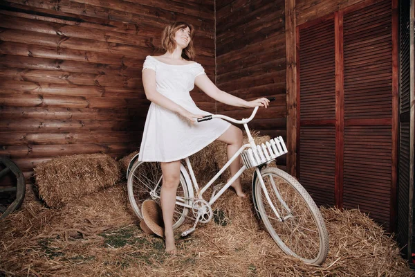Piękna dziewczyna w białej sukni letniej pozuje z rowerem w sianie po jesiennych zbiorach — Zdjęcie stockowe