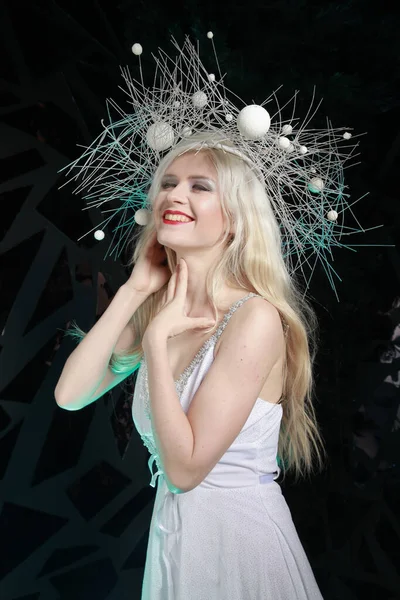 Hot strange slender woman with long blonde hair wearing white dress and unusual hat on black background alone — ストック写真