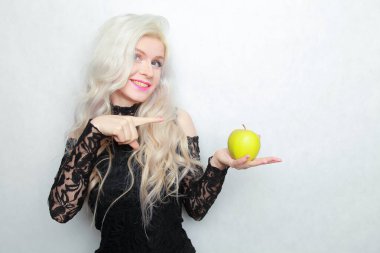 Süslü, siyah elbiseli, beyaz arka planda yeşil elmalı genç bir kadın stüdyoda.