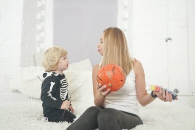 Anne ve çocuk kanepede oturan beyaz oda arka planında birlikte balkabağı boyuyorlar.