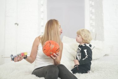 Anne ve çocuk kanepede oturan beyaz oda arka planında birlikte balkabağı boyuyorlar.