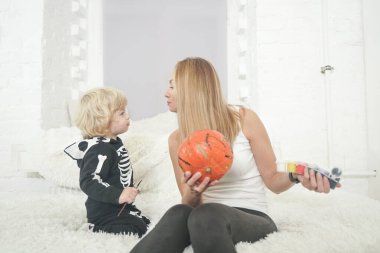 Anne ve çocuk kanepede oturan beyaz oda arka planında birlikte balkabağı boyuyorlar.