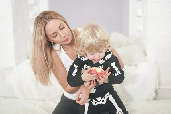 Mãe e filho criança se divertindo com saborosos donuts doces dentro de casa. menino no halloween esqueleto traje jogar com linda mãe . — Fotografia de Stock