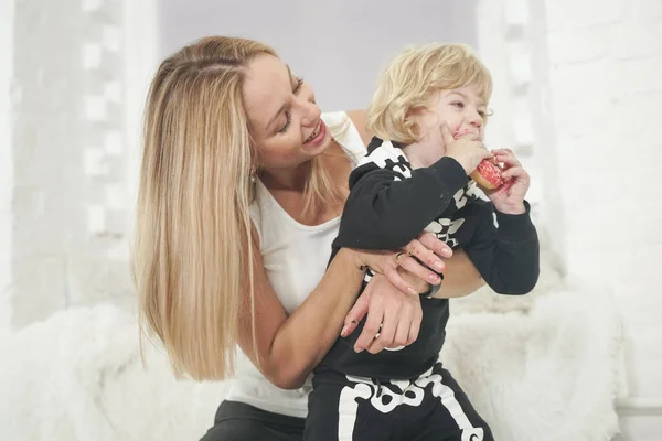 Mother and son child having fun with tasty sweet donuts indoors. Boy in halloween skeleton costume playing with lovely mom. — Stock Photo, Image