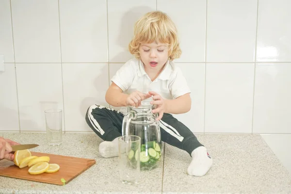 Πορτρέτο μιας αξιολάτρευτης μητέρας και του μικρού παιδιού προετοιμασία ένα ποτό φυτικό νερό μαζί στη λευκή κουζίνα — Φωτογραφία Αρχείου