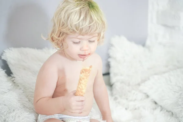 Μικρό παιδί που παίρνει βάφλα και την τρώει με ευχαρίστηση και διασκέδαση σε λευκό φόντο δωματίου — Φωτογραφία Αρχείου