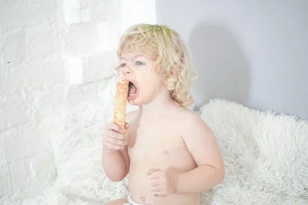 Маленька дитина бере вафельку і їсть її з задоволенням і весело на фоні білої кімнати — стокове фото