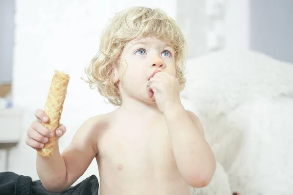 Pequena criança tomando waffle e comê-lo com prazer e diversão no fundo da sala branca — Fotografia de Stock