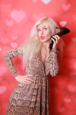 Genç bir kadının ayakkabıyı yüzüne yakın tutan bir telefon gibi kullanması ve konuşması, kırmızı arka plan. Pin-up tarzı.