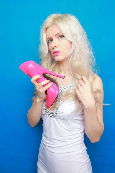 Hermosa chica modelo joven sostiene un zapato rosa caliente lacado y disfruta sobre un fondo azul en el estudio. concepto fetiche tacones altos. ventas de calzado — Foto de Stock
