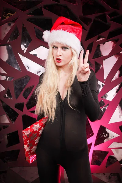 Boldog aranyos karcsú fiatal nő karácsonyi szőrme kalap kezében ajándék doboz sötét nightclub háttér. rossz játékos Mikulás lány. — Stock Fotó