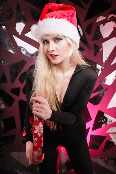 Felice carino snello giovane donna in cappello di pelliccia di Natale contenente scatola regalo su sfondo discoteca scuro. cattivo giocoso Santa ragazza . — Foto Stock