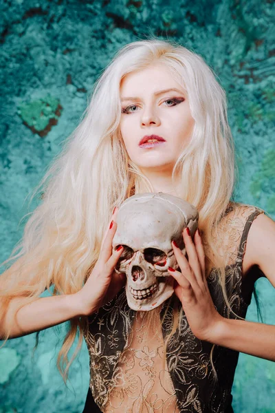 Krásná žena s blond účesem. dospělá štíhlá dívka s halloween lebkou v rukou. mystické světlo. — Stock fotografie
