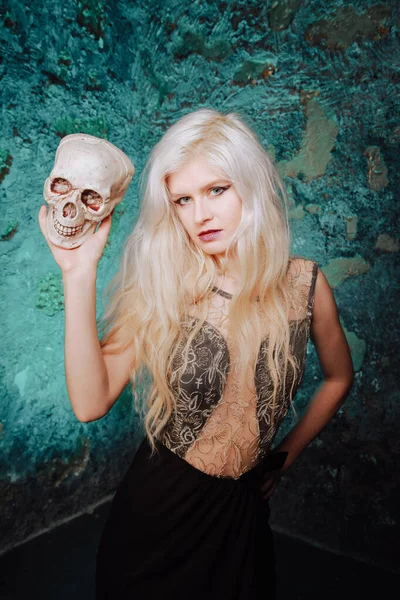 Krásná žena s blond účesem. dospělá štíhlá dívka s halloween lebkou v rukou. mystické světlo. — Stock fotografie