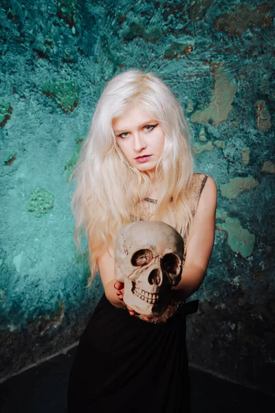 Krásná žena s blond účesem. dospělá štíhlá dívka s halloween lebkou v rukou. mystické světlo. — Stock fotografie