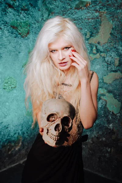 Beautiful woman with blond hairstyle. adult slim girl with halloween skull in hands. mystic light. — ストック写真