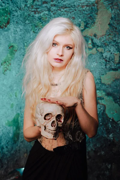 Beautiful woman with blond hairstyle. adult slim girl with halloween skull in hands. mystic light. — ストック写真