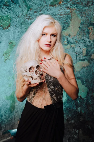 Mulher bonita com penteado loiro. menina magro adulto com crânio halloween nas mãos. luz mística . — Fotografia de Stock
