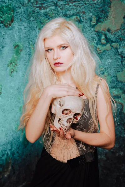 Beautiful woman with blond hairstyle. adult slim girl with halloween skull in hands. mystic light. — ストック写真