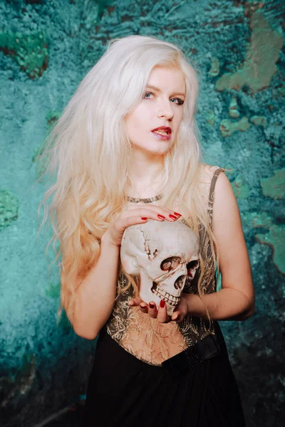 Belle femme aux cheveux blonds. adulte mince fille avec crâne d'Halloween dans les mains. lumière mystique . — Photo
