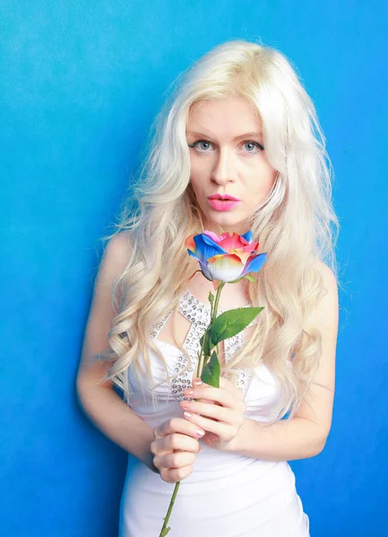 Mignonne fille blonde ludique en robe blanche se tient avec eco friendly rose artificielle sur fond bleu dans Studio — Photo