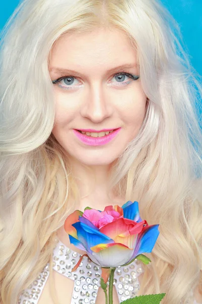 Schattig speels blond meisje in witte jurk staat met eco vriendelijke kunstmatige roos op blauwe achtergrond in Studio — Stockfoto