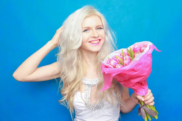Mulher tipo feliz quente em vestido de moda apertado branco com flores de tulipa rosa no fundo do estúdio azul . — Fotografia de Stock