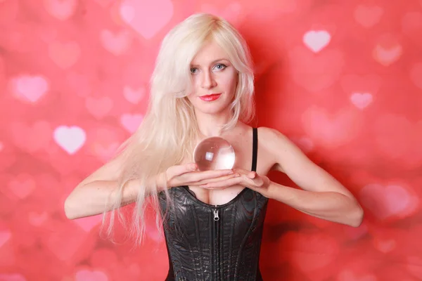 Magische jonge vrouw met grote kristallen bal en willen weten de toekomst van de liefde op rode studio achtergrond — Stockfoto