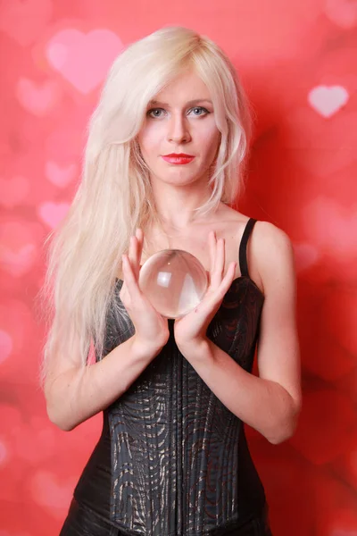 Magia jovem segurando grande bola de cristal e quer saber o futuro do amor no fundo do estúdio vermelho — Fotografia de Stock