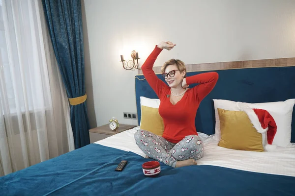 Χαριτωμένο συν μέγεθος κοντά μαλλιά ξανθιά κοπέλα σε γυαλιά χασμουρητό το πρωί στο κρεβάτι κάθεται με πιτζάμες και τεντώνει — Φωτογραφία Αρχείου