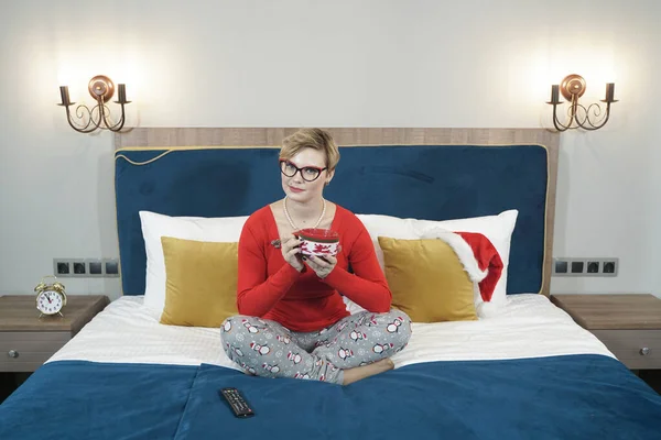 Krásná žena s šálkem kávy sedí na posteli ve své ložnici — Stock fotografie