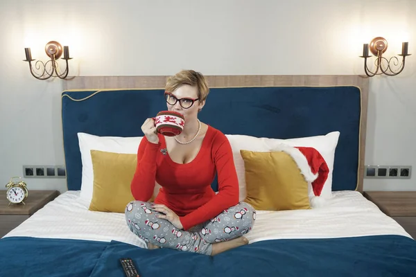 Όμορφη γυναίκα με φλιτζάνι καφέ κάθεται στο κρεβάτι στην κρεβατοκάμαρά της — Φωτογραφία Αρχείου