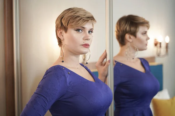 A bela jovem com figura curvilínea e cabelo curto em vestido de moda perto do espelho — Fotografia de Stock