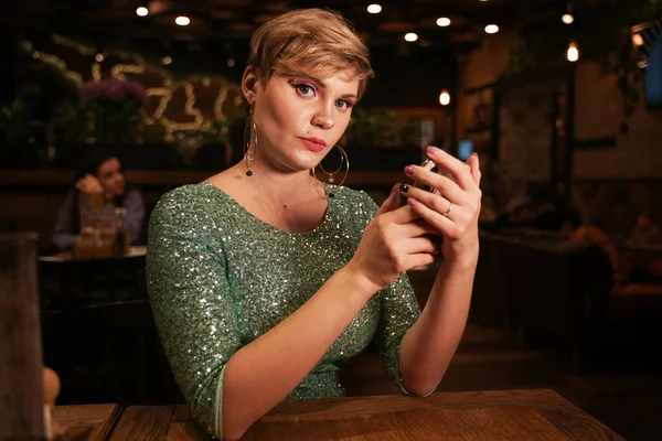 Mujer bonita con teléfono inteligente en la cafetería de la noche — Foto de Stock