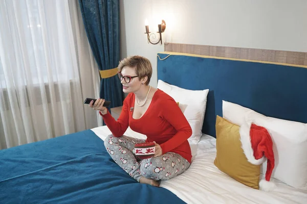 Mladá žena v červené vánoční svetr sledování televize na posteli — Stock fotografie