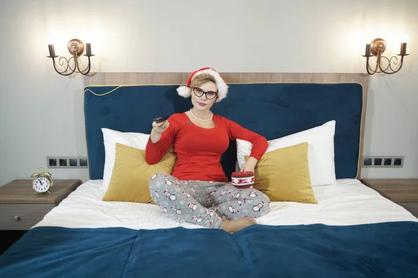 Jeune femme en pull de Noël rouge regardant la télévision sur le lit — Photo