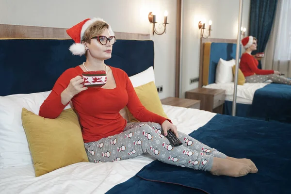 Jeune femme en pull de Noël rouge regardant la télévision sur le lit — Photo