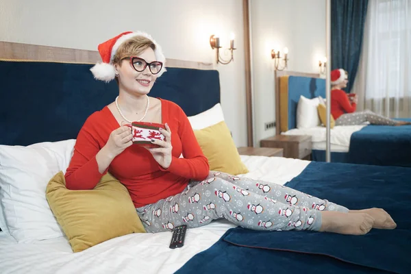 Jeune femme en pull de Noël rouge regardant la télévision sur le lit — Photo