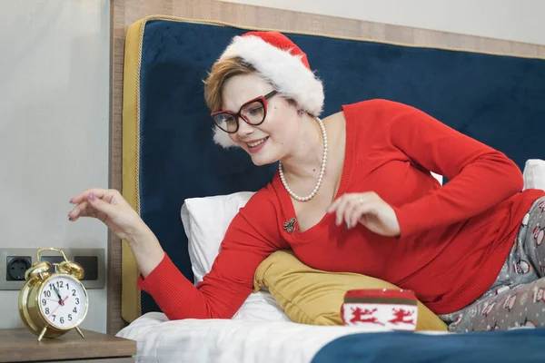 Plus size kobieta w kapeluszu Santa ze złotym budzikiem retro w sypialni — Zdjęcie stockowe