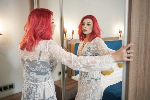 Hermosa novia chica con rojo bob corte de pelo en encaje vestido largo posando en su dormitorio solo cerca del espejo —  Fotos de Stock