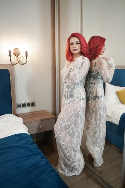 Vacker brud flicka med röd bob frisyr i spets lång klänning poserar i hennes sovrum ensam nära spegeln — Stockfoto