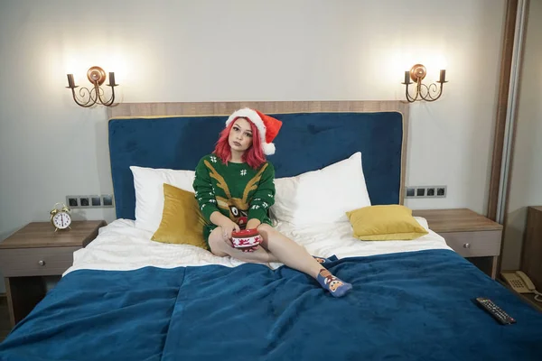 Santa femme en chapeau rouge et pull oversize de Noël sur le lit se détendre après la fête — Photo