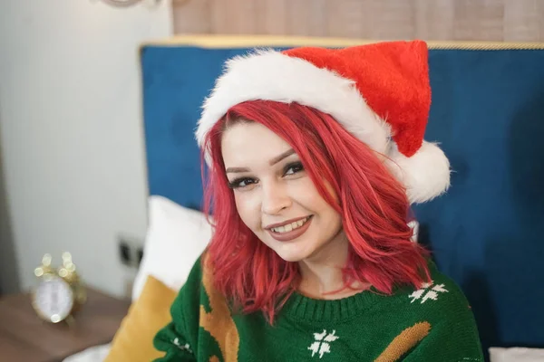 Santa woman in red hat and christmas oversize sweater on the bed relax after party — Stock Photo, Image