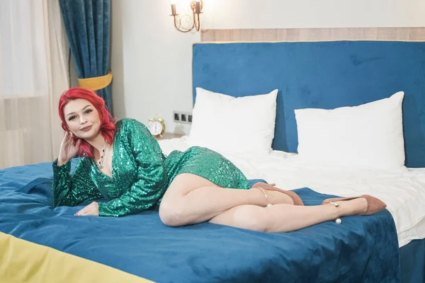 Yeşil şık, ışıltılı elbisesi olan seksi kadın Noel partisine hazır ve yatağında yalnız başına bekleyerek rahatlıyor. — Stok fotoğraf