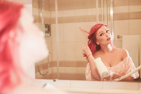 Ung vacker kvinna med hårtork tittar på spegeln i badrummet — Stockfoto