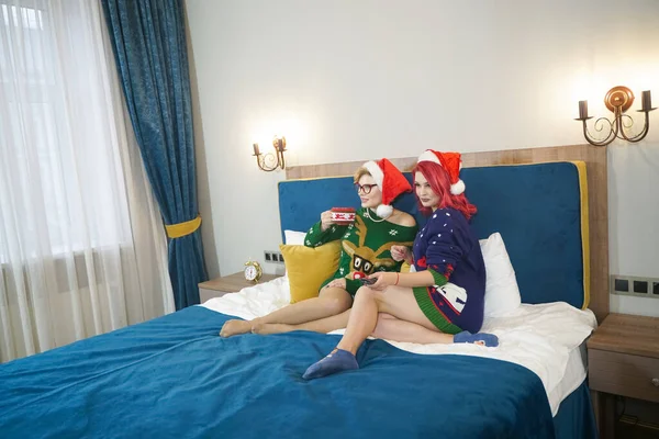 Yılbaşı arifesinde yatak odasında Noel süveteri giymiş iki genç kadının kapalı mekan portresi. Gülümsüyor, eğleniyor, kutlamaya hazır. En iyi arkadaşların parlak tatil imajı. — Stok fotoğraf