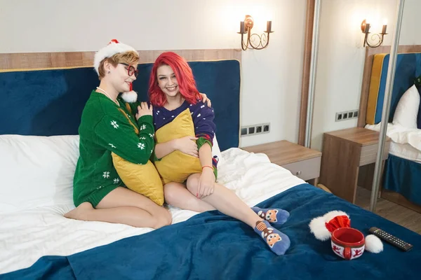 Dwie ładne dziewczyny siedzące na łóżku i przytulające się na święta — Zdjęcie stockowe