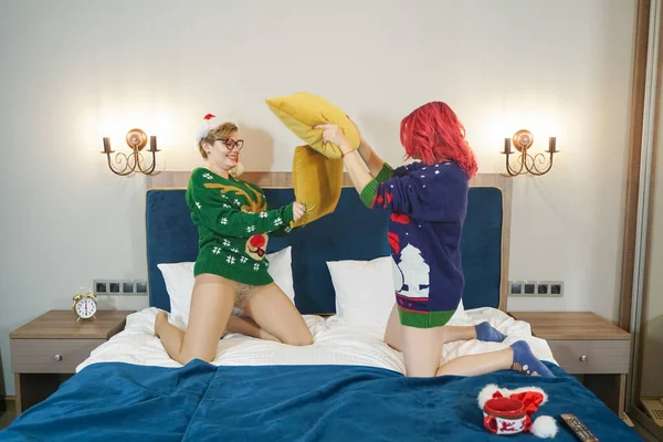 Due simpatici amici ragazze felici hanno lotta cuscino in maglioni di Natale sul grande letto blu — Foto Stock